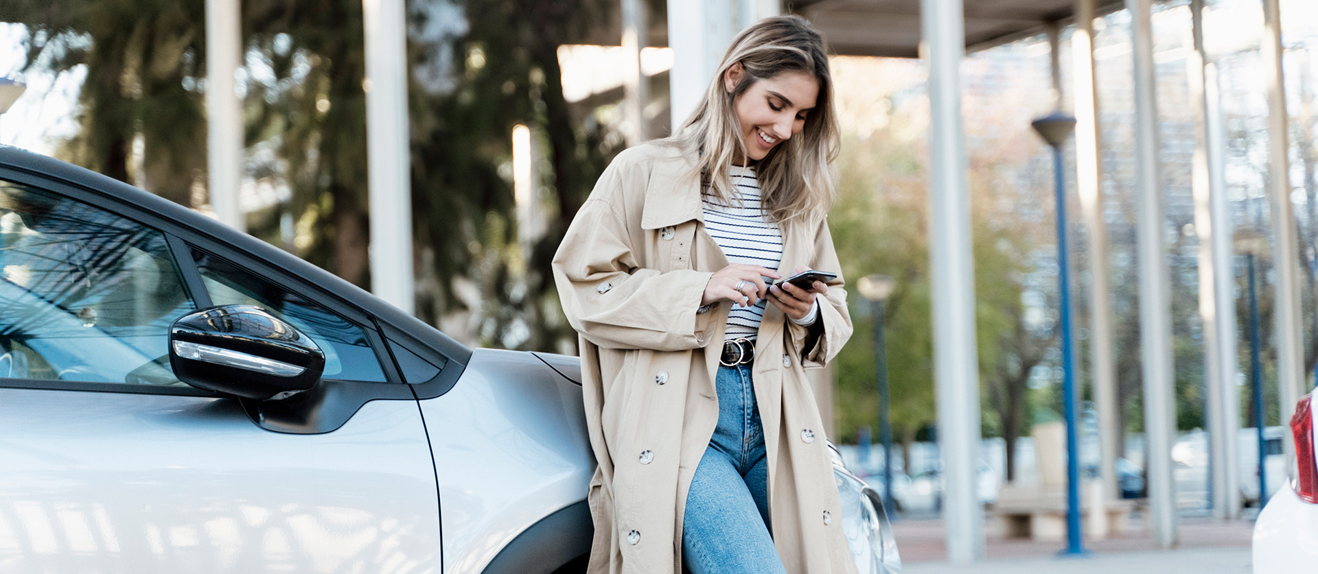 Vrouw leunt tegen haar motorkap aan met een smartphone in der hand