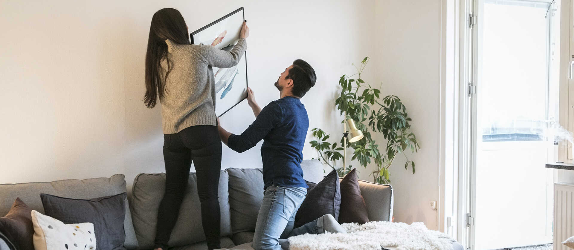 een jong stel hangt samen een schilderij op achter de bank